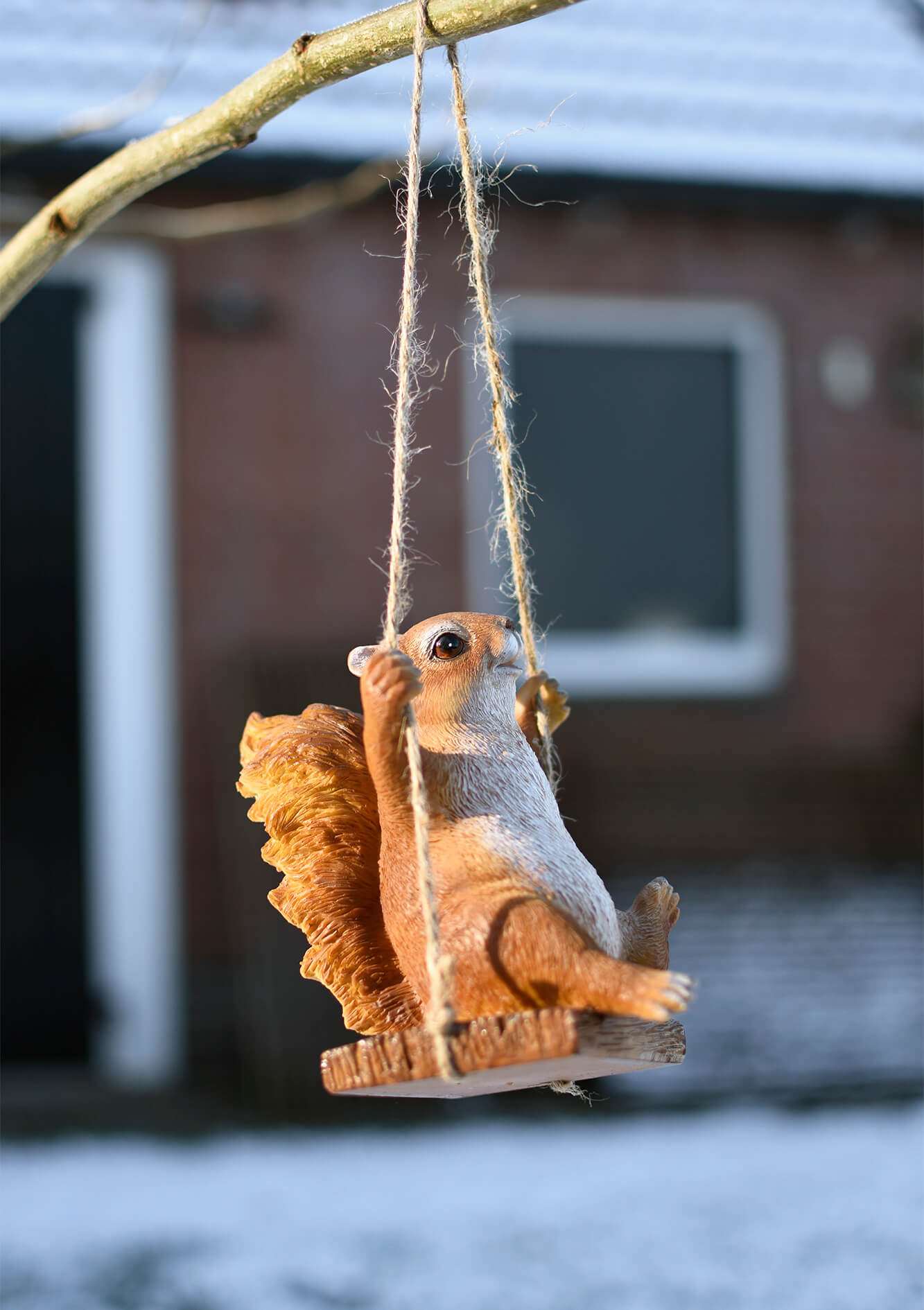 Tuinbeeldje van een eekhoorn op een schommel.
